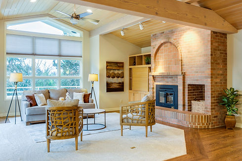 Renovated living room with brick fireplace, exposed wood ceiling, large windows, and modern seating in a Charleston home renovation.