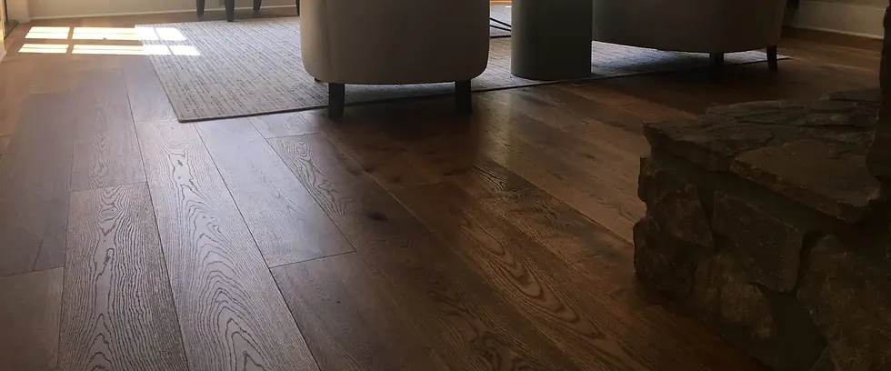 Dark wide plank wood flooring in living room with sunlight, area rug, and upholstered chairs.
