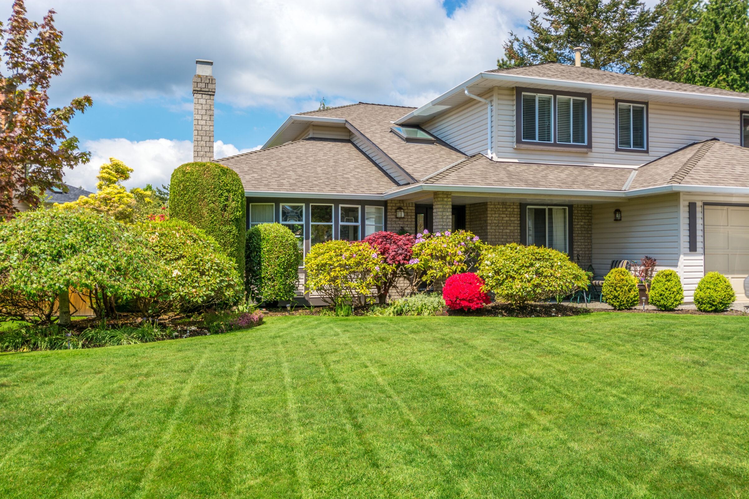 Freshly mowed residential lawn with trimmed shrubs and colorful landscaping maintained through routine lawn care services in Western North Carolina.