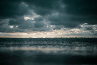 A choppy, dark moody sea stretches back towards a bright horizon which sits behind a thick layer of dark threatening clouds