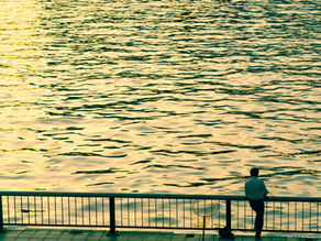 man standing next to fence by lake at sunset