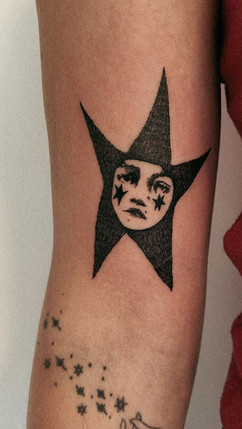Чорна зірка з обличчям у центрі — символічне татуювання з ретро-настроєм.