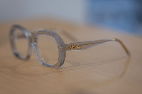 Lunettes de vue Prada, monture claire élégante, posées sur table en bois.