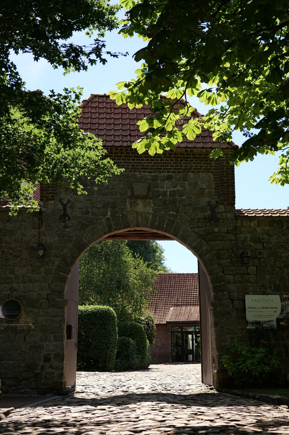 Porche en pierre et en briques ouvrant sur la cour pavée de La Ferme de la Motte Dorée.