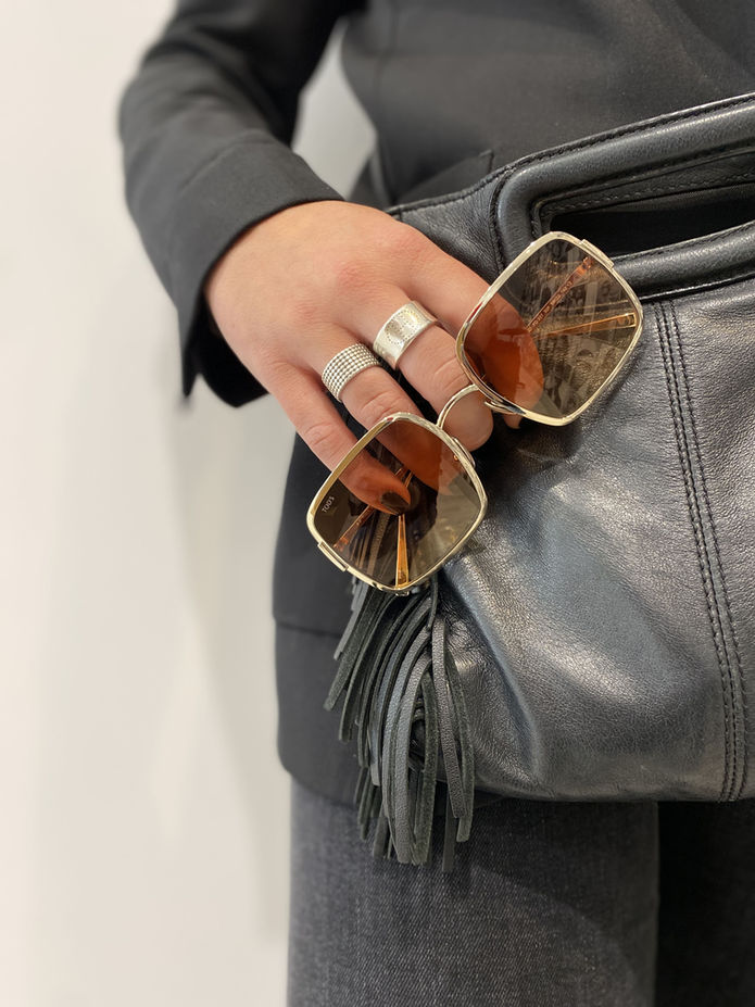 Main tenant des lunettes de soleil dorées, verres fumés, sur un sac noir.