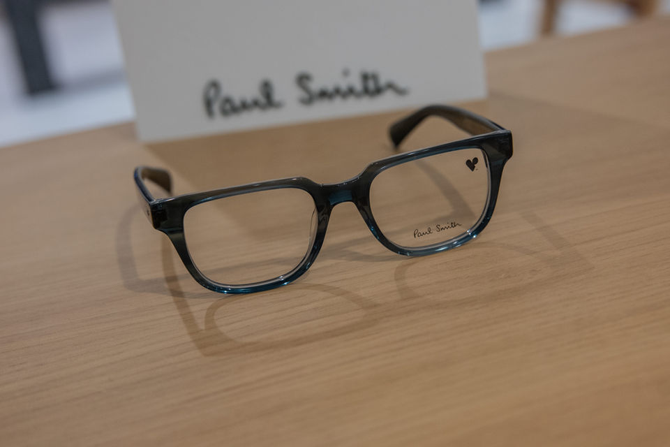 Lunettes de vue Paul Smith noires, posées sur une table en bois.