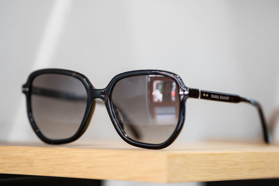 Lunettes de soleil noires avec texte ISABEL MARANT posées sur étagère en bois.