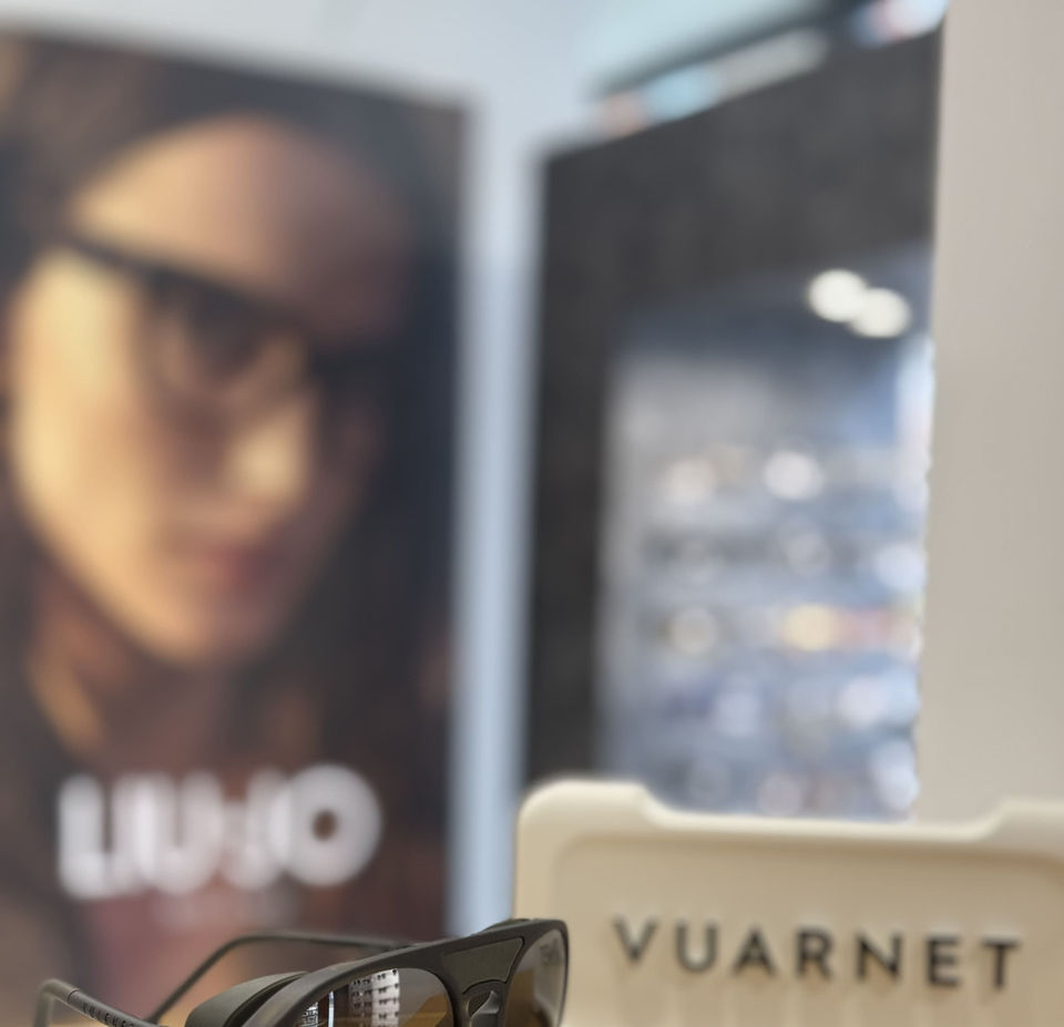 Lunettes de soleil noires Vuarnet sur présentoir, texte Luxo derrière.