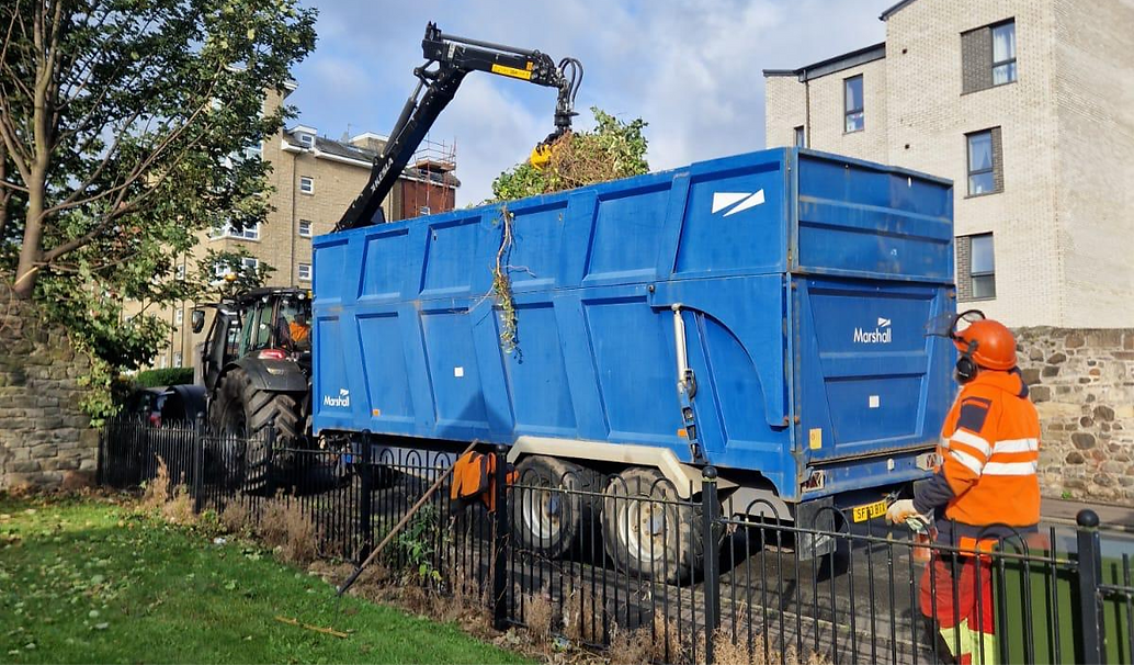 Large blue Marshall waste container and forestry crane equipment parked outside a building during site clearance