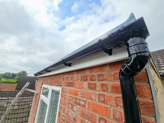 Black guttering and downpipe installed on a brick house.