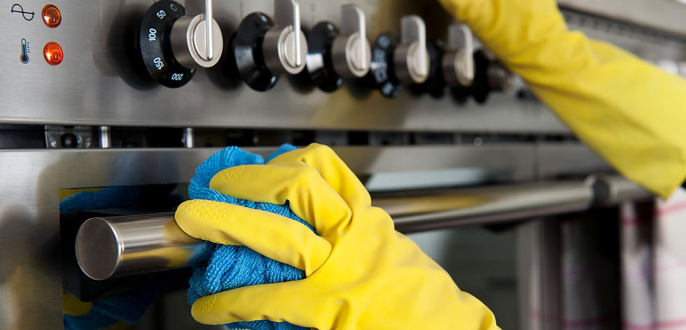 Close-up view of a hand wearing a yellow rubber glove wiping down a stainless steel oven door handle with a blue microfiber cloth