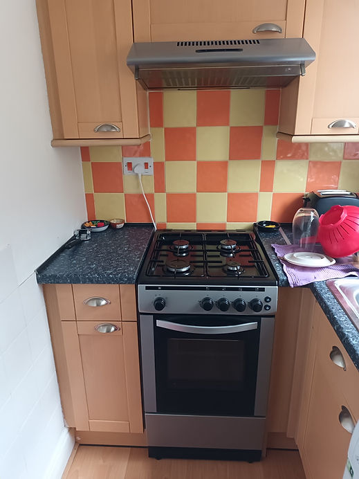 Freestanding black gas cooker with oven and hob installed between kitchen cabinets against a orange and cream tiled splashback