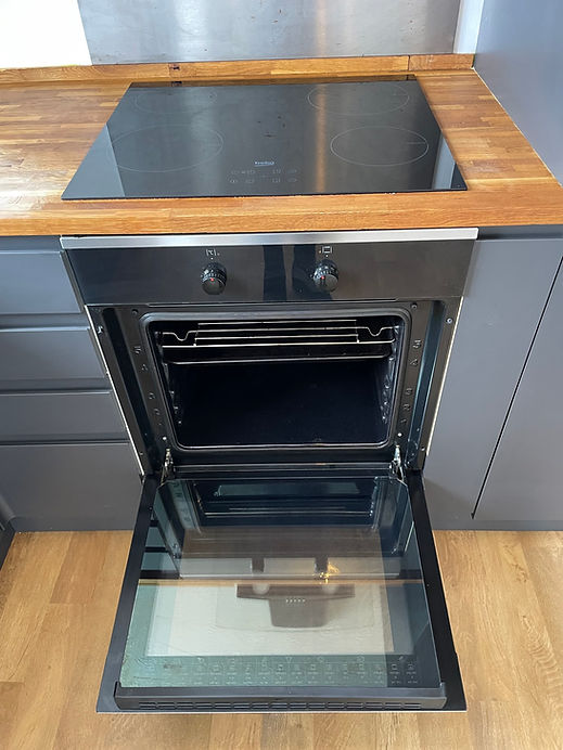 Modern built-in stainless steel oven with its door wide open, fitted beneath a dark ceramic hob in a modern kitchen unit