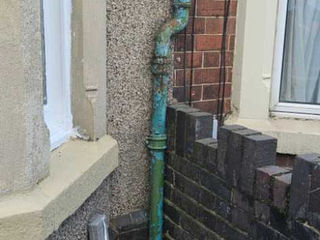 Green vertical drainage pipe against a brick wall exterior.