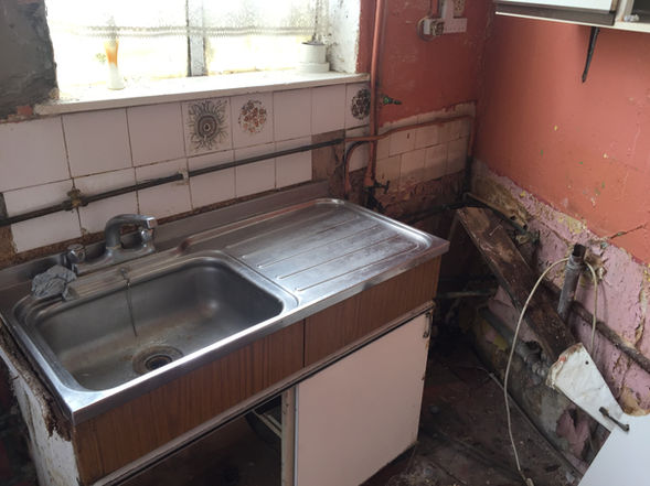 Kitchen area with sink, cupboards and tiled splashback