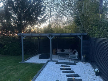Landscaped garden featuring grey decking, white gravel path, and a modern timber pergola with seating.