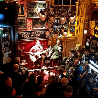 Live music in Temple Bar with a packed crowd enjoying a band performance at The Merchant's Arch. People are seated and standing around tables in a lively night-time setting.