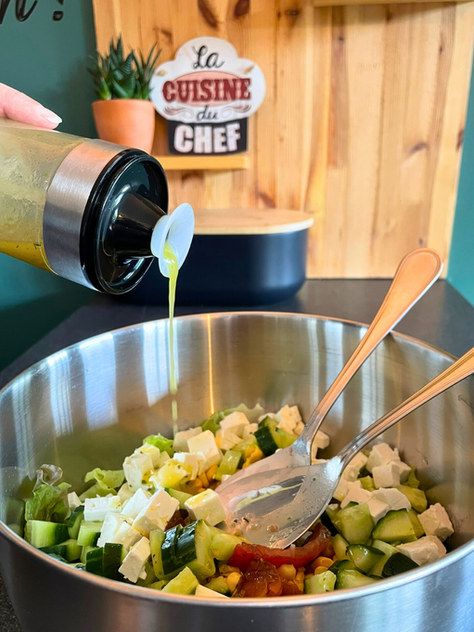 Vinaigrette citronnée au miel versée depuis un shaker NICO® dans une salade estivale avec feta, concombre et maïs, dans une cuisine familiale artisanale.