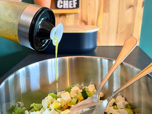 Vinaigrette citronnée au miel versée depuis un shaker NICO® dans une salade estivale avec feta, concombre et maïs, dans une cuisine familiale artisanale.