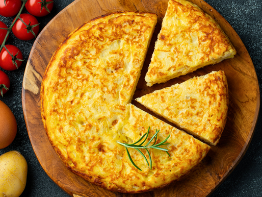 Tortilla de patatas maison dorée servie sur une planche en bois, entourée d’ingrédients frais : tomates cerises, pommes de terre, oignons jaunes, œufs et herbes aromatiques – recette espagnole traditionnelle simple et sans viande.