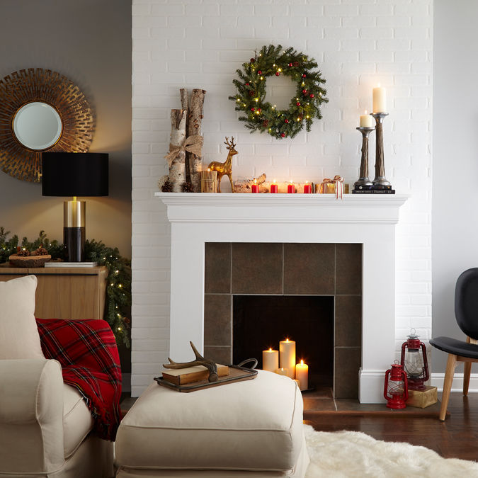 Holiday scene with a neutral chair, fireplace with lit candles, and holiday decor