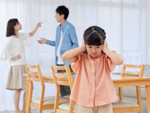 Young girl in distress covering her ears while parents argue in the background, showing the impact of parental conflict and emotional abuse on children.