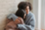Two women sitting together in a comforting embrace, offering emotional support in a moment of vulnerability, with a soft, natural light highlighting their connection.