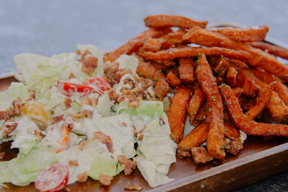 Crisp salad with creamy dressing, cherry tomatoes and bacon bits beside a pile of seasoned sweet potato fries on a wooden tray at The Farmer's Daughter.