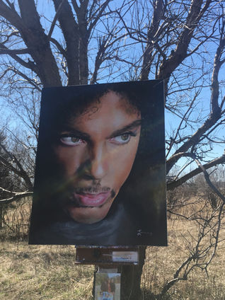 Still from Dearly Beloved (2026): Photograph of Dan Lacey's painting of Prince positioned in front of a tree, with branches extending behind and above the painting against a blue sky