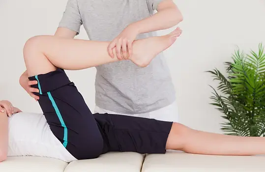 Masseuse stretching the right leg of a young woman.webp