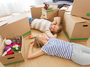Zwei junge Menschen, die zwischen Umzugskartons am Boden liegen und sich anlächeln