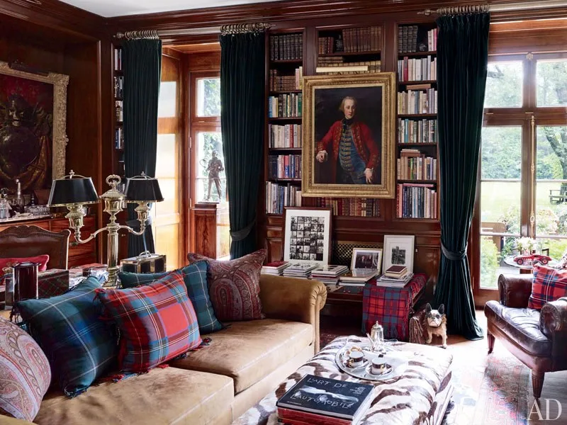 An old-money aesthetic living room with artwork, books, plaid pillows layered over velvet cushions, and dark drapes