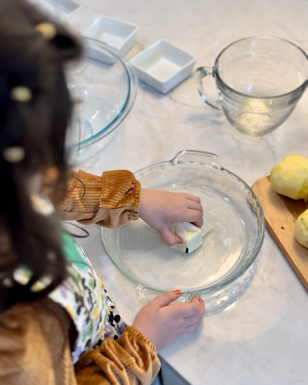 A little girl spreading butter in a glass pie dish