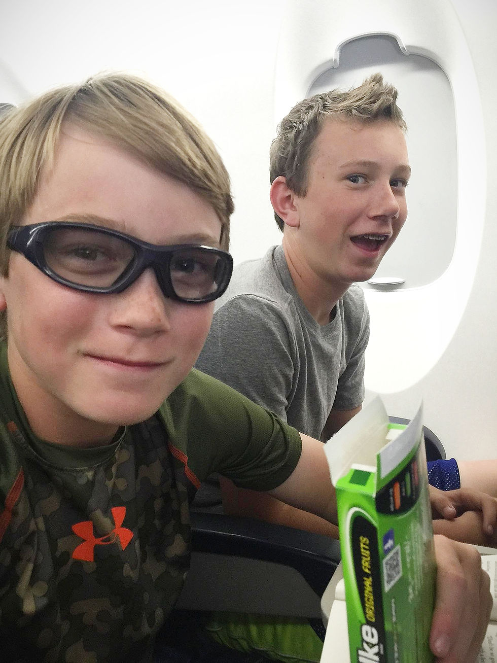 Two young boys sitting together on an airplane enjoying a special snack