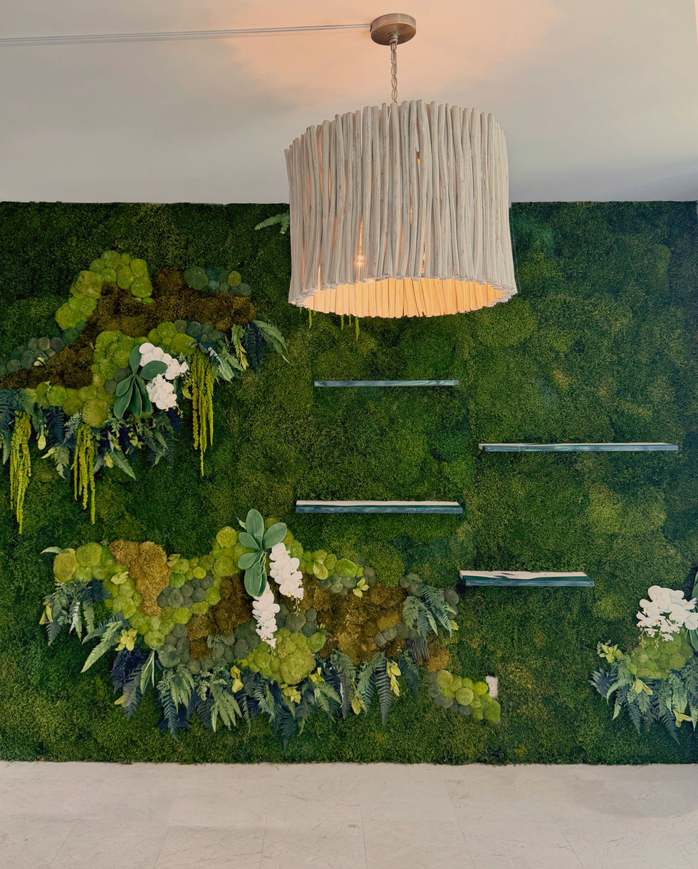 A medium-view photograph of a multi-dimensional preserved moss wall installation featuring rich green textures and blooming white orchid accents.