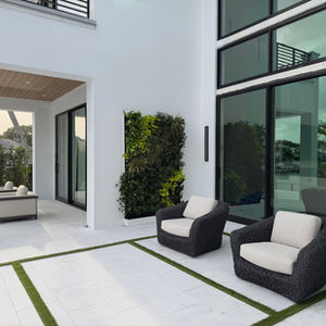 A wide view of a luxury modern white house patio in Jupiter, Florida, featuring a custom exterior living green wall between large black-framed glass doors and outdoor armchairs