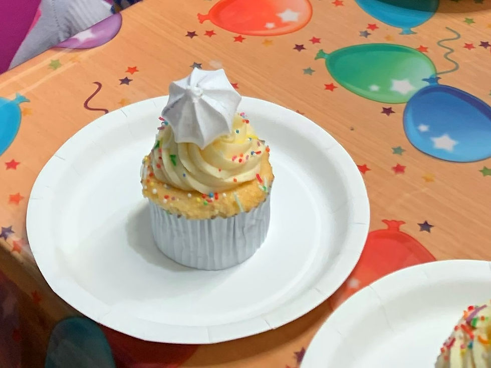 cupcake in a silver paper liner topped with a meringue drop, vanilla buttercream icing and rainbow sprinkles.