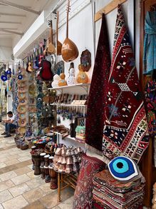 An authentic Turkish souvenir shop showcasing a rich array of cultural artifacts, including traditional string instruments, vibrant handmade carpets, and colorful evil eye bead ornaments. The shop offers a variety of crafts and textiles, reflecting the country's rich heritage and craftsmanship, perfect for tourists seeking to take a piece of Turkey's cultural legacy home.