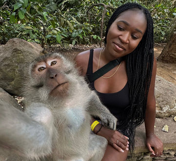 An engaging and candid moment captured with a woman smiling beside a curious macaque in a lush forest sanctuary, highlighting the close interaction between humans and wildlife in natural settings.
