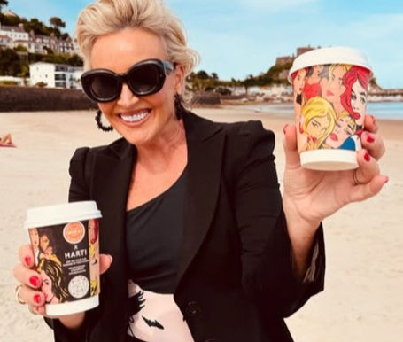 Tessa Hartmann in Harti Swimwear holding a Cooper & Co coffee cup featuring pop art design.