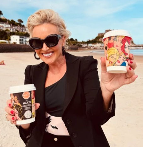 Tessa Hartmann in Harti Swimwear holding a Cooper & Co coffee cup featuring pop art design.