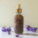 Speckled purple liquid in glass dropper bottle with scattered violet flowers.
