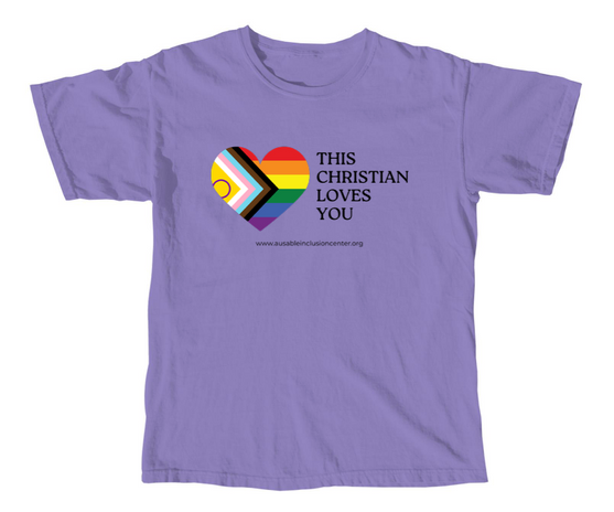 A lilac shirt with a progress pride flag heart and the words "This Christian Loves You." Under the body of the text and the heart is the web address "www.ausableinclusioncenter.org"