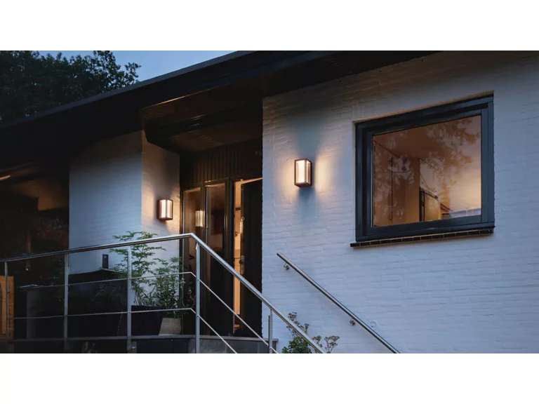 Philips Hue Impress Outdoor Wall Light installed on white brick exterior near a front door, adding smart curb appeal lighting.