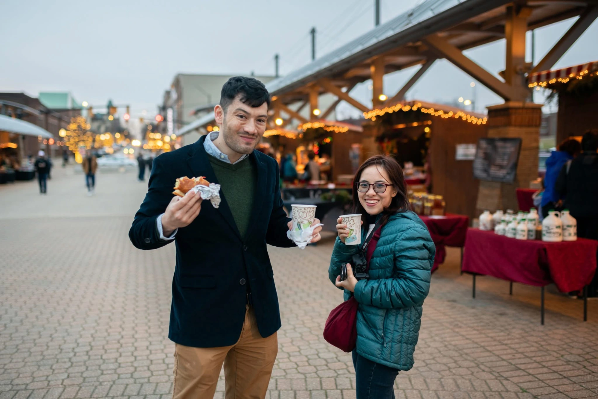 Couple enjoying hot coffee and fresh donuts while shopping local vendors at the Kerstmarkt Christmas market in Holland, MI.