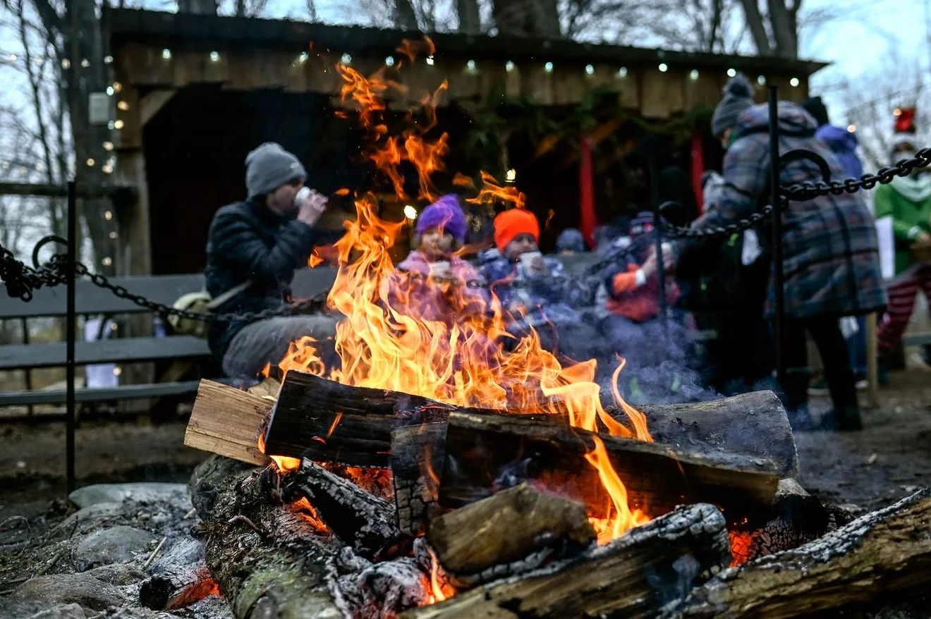 Visitors sip hot chocolate and roast marshmallows around a crackling outdoor fire, creating cozy holiday memories at Peacock Road Family Farm’s Christmas festivities.