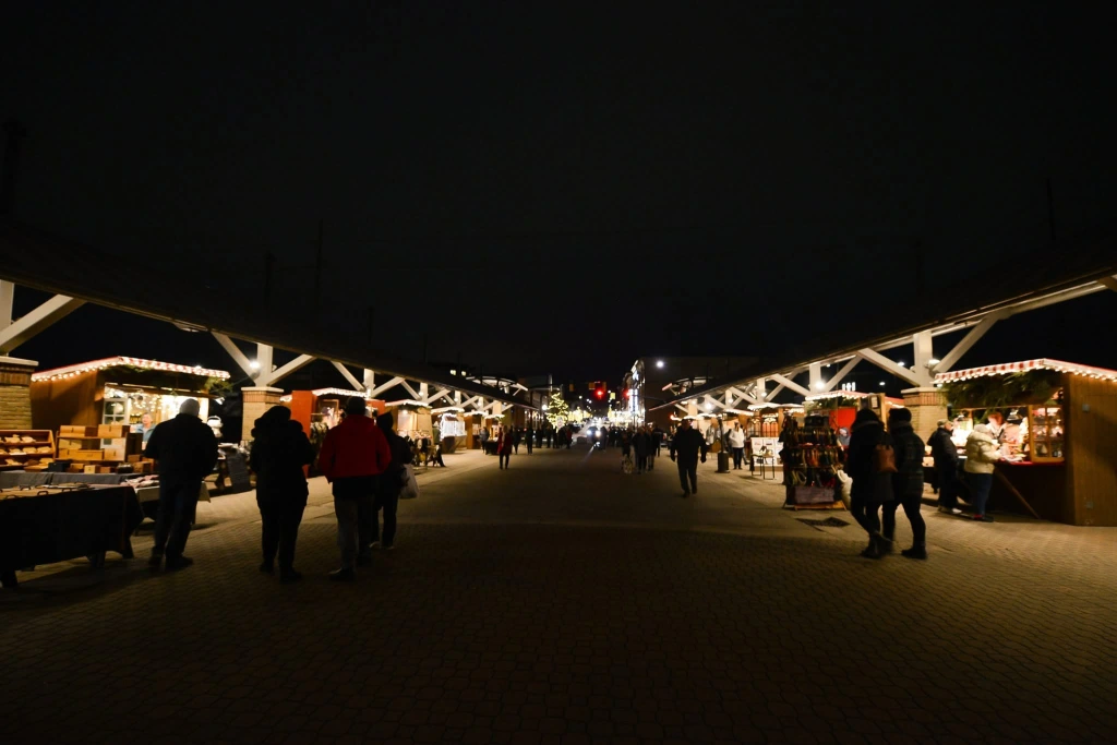 Twinkling holiday lights illuminate the Kerstmarkt in downtown Holland, MI at night, with festive vendor booths lining the street.