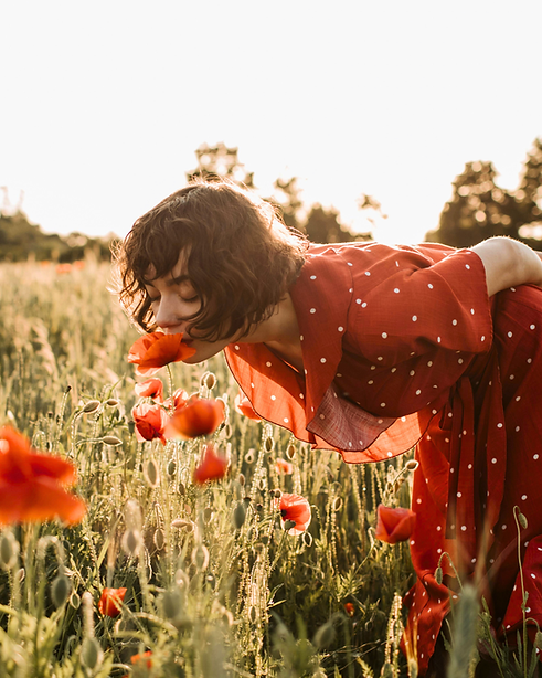 Woman in red dress smelling poppies in sunset field