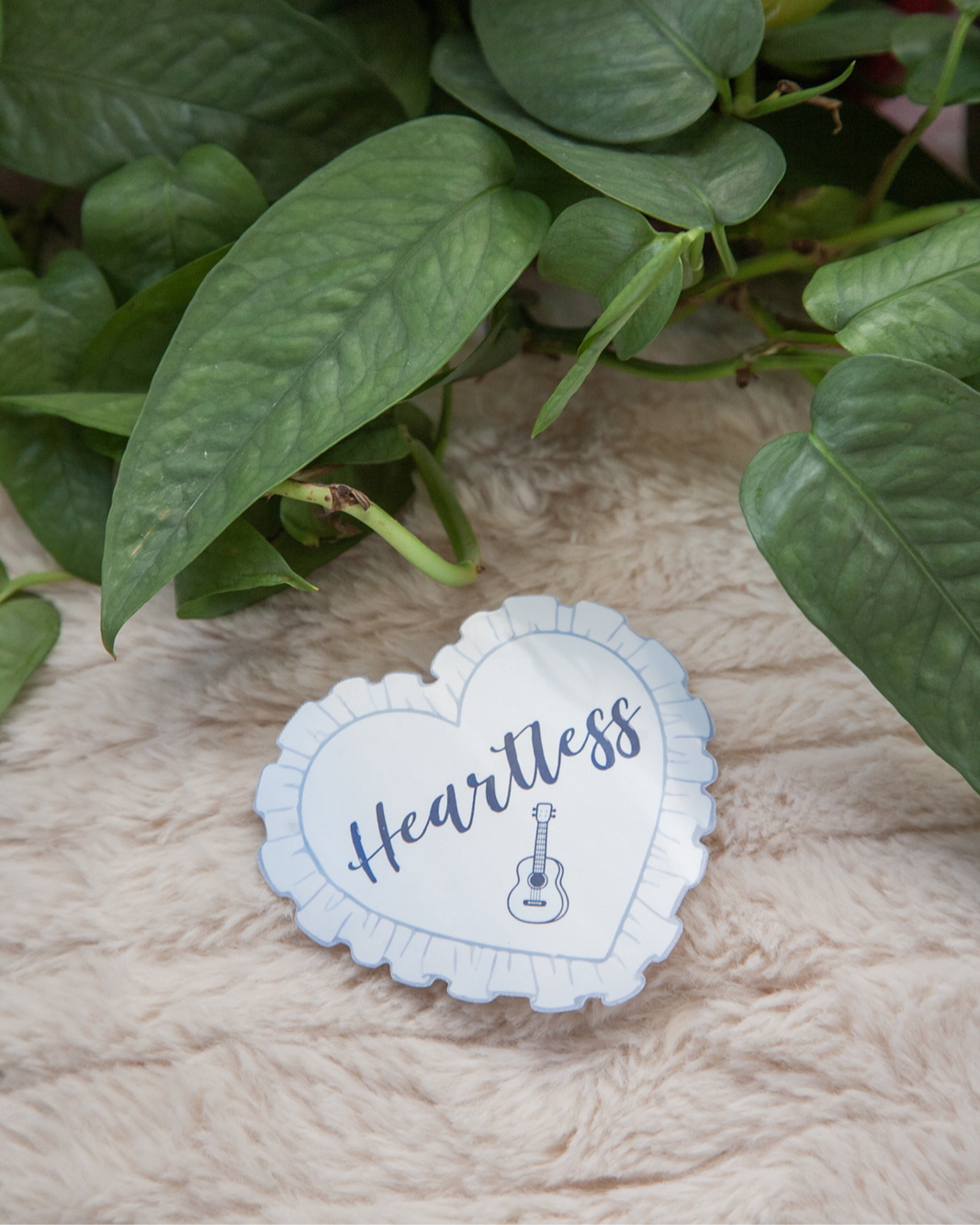 Light pastel blue heart sticker with the words heartless and a small simple guitar drawing underneath