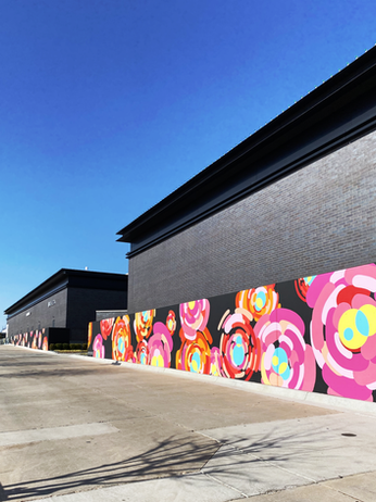 Large-scale public mural featuring colorful abstract rosettes inspired by Oklahoma's state rock, the rose rock, installed at Classen Curve in Oklahoma City.
